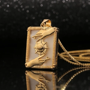 Gold rectangular pendant necklace with shell eye design and box chain on black mirror surface