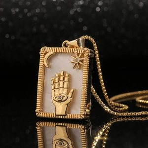 Gold Hamsa tarot pendant necklace with shell inlay and star details on black background