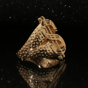 Macro shot of gold hip hop ring with dollar sign and hammered texture on black mirror