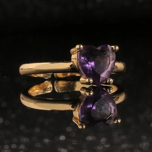 Gros plan d'une bague de cœur dorée avec une pierre violette sertie de quatre griffes