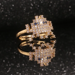 Bague alien pixel dorée avec zircons blancs et bleus sur surface réfléchissante noire