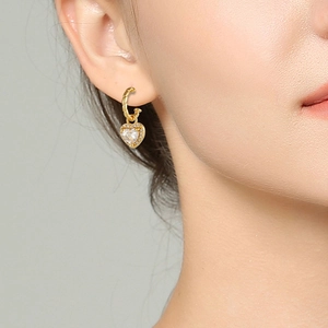 Detailansicht eleganter goldener Herzohrringe mit Zirkonia am Ohr eines Models