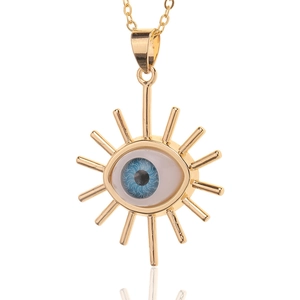 Detail of gold-plated evil eye pendant with blue resin and sunburst lines on white background