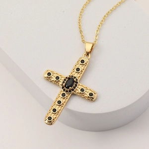 Collana a croce placcata oro 18K con pietre nere su un supporto espositivo bianco