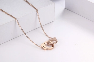 Close-up of rose gold handcuff pendant with crystal accents on a white geometric stand