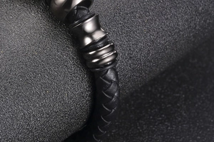 Macro detail of men's black woven leather bracelet with gunmetal bead on grey fabric