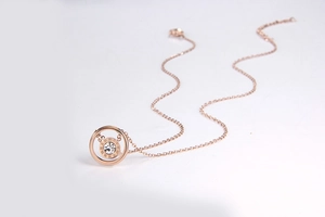 Macro detail of rose gold necklace with double ring pendant and Roman numeral engraving