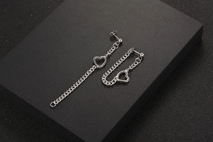 Détail macro de boucles d'oreilles asymétriques en acier titane avec chaîne et pendentif cœur