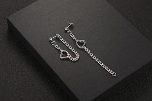 Détail de boucles d'oreilles asymétriques en acier titane avec cœur et chaîne