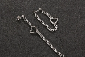 Gros plan de boucles d'oreilles argentées asymétriques avec chaînes fines et coeurs creux