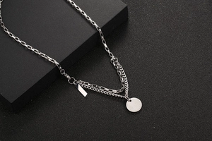 Detail of silver double-layered titanium steel necklace with circular pendant on black background