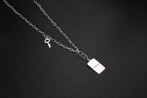Detalle macro del collar plateado con placa grabada THE SOUL y colgante de llave