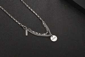 Detail of layered titanium steel necklace featuring an engraved round coin and rectangle tag