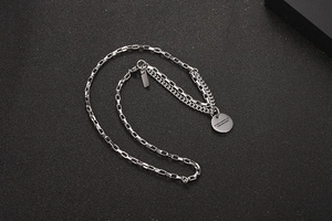 Detail view of silver layered box and curb chains with engraved round metal pendant