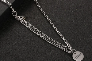Detail of layered titanium steel necklace with engraved round tag and mixed box curb chains