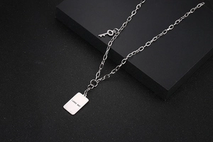 Detalle del collar plateado con dije de llave y grabado sobre un soporte negro mate