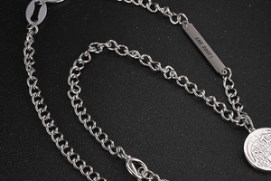 Detailed close-up of silver metal chain necklace with THE SON rectangular tag and round pendant