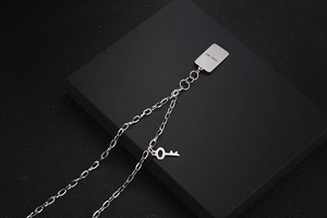 Detalle de collar de cadena plateada con placa rectangular y colgante de llave