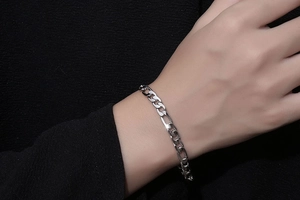 Close-up of polished silver Figaro chain bracelet worn on wrist over black background