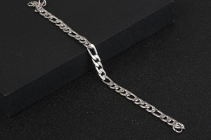 Detailed close-up of a silver Figaro chain bracelet featuring polished steel links on a black stand
