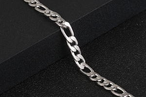 Close-up of a polished silver Figaro chain bracelet on a black textured surface