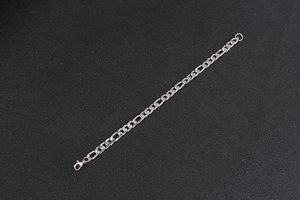 Detailed view of silver Figaro chain bracelet with lobster clasp on dark background