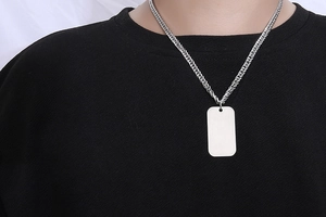 Close-up of polished silver rectangular pendant with thick wheat chain on black shirt