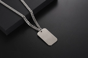 Close-up of a silver stainless steel dog tag pendant with a chunky Cuban link chain necklace