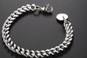 Vue macro du bracelet à mailles cubaines en acier poli avec fermoir mousqueton et pendentif