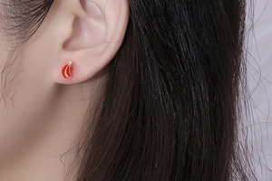 Close-up of small red and gold curved leaf stud earrings worn on a female ear