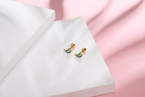 Detailed close-up of gold banana-shaped stud earrings on white marble with pink silk