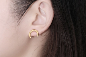 Gros plan d'une boucle d'oreille croissant de lune dorée portée sur le lobe