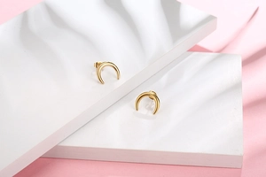 Gros plan de boucles d'oreilles lune dorées polies sur des socles minimalistes