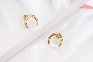 Gros plan de boucles d'oreilles croissants de lune dorés sur un fond blanc minimaliste