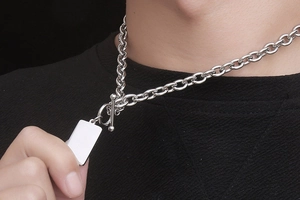 Detalle de cadena de acero de titanio plateado con cierre OT y colgante sobre negro