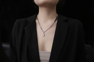 Dettaglio di una collana con ciondolo a lucchetto asimmetrico indossata su un blazer nero