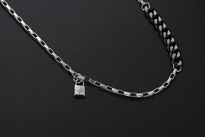 Dettaglio macro della collana asimmetrica con catena argento, maglie nere e ciondolo a lucchetto