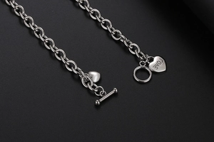 Macro-detail van zilveren hartjeshangers met LOVE-gravure en T-sluiting aan de ketting