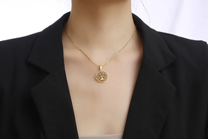 Detailopname van de gouden Levensboom-ketting gedragen door een model in een zwart jasje