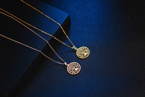 Detailopname van levensboom hangers in goud en roségoud op een blauwe achtergrond