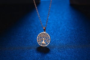 Detailopname van de roségouden Levensboom hanger met fijne ketting op blauwe basis