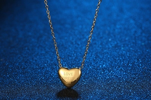 Detailed view of golden heart-shaped necklace with Love Forever 520 engraving on blue background