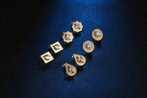Dettaglio di cinque paia di orecchini d'oro con zirconi e perle su sfondo blu navy