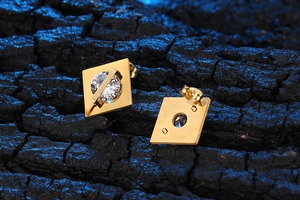 Macro di orecchini a perno quadrati dorati geometrici con zirconi su legno scuro