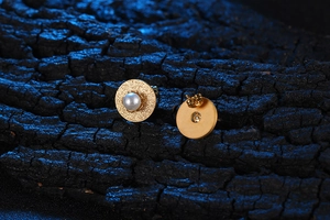 Dettaglio macro di orecchini a perno in oro satinato con perla e chiusura a farfalla