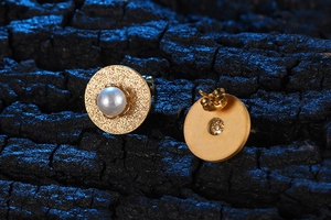 Dettaglio di orecchini vintage in oro opaco con perla centrale su legno strutturato