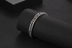 Detailed view of polished silver Cuban link bracelet displayed on black cylindrical stand
