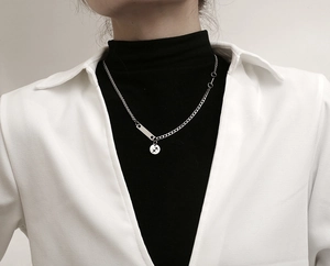 Detalle de collar de titanio plateado con dije de Sagitario y colgante de barra metal