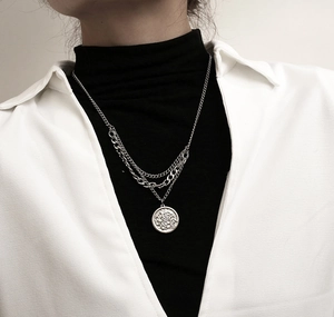 Close-up of layered titanium steel necklaces with round coin pendants on a model