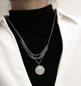 Close-up of layered silver titanium steel necklace with a round embossed coin pendant